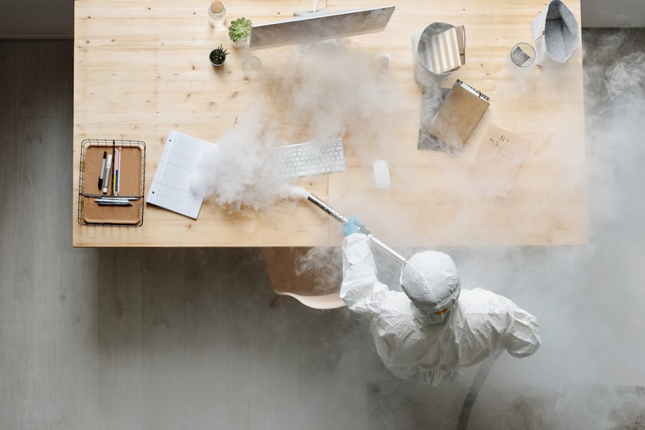 An individual disinfects a workspace using fumigation, wearing full protective gear for safety.